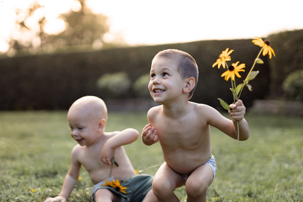Un niño y un bebé jugando con flores amarillas en el jardín