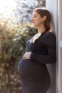 Retrato de maternidad de una mujer embarazada disfrutando del sol primaveral con los ojos cerrados.